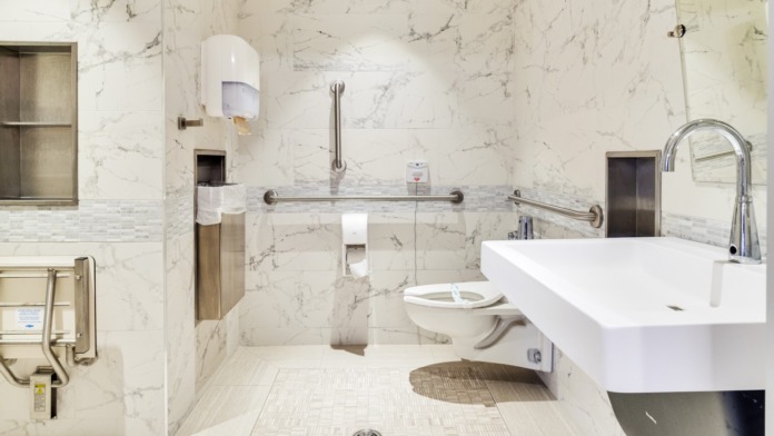 Modern bathroom with marble-effect tile walls, white rectangular sink, grab bars, and accessible features.