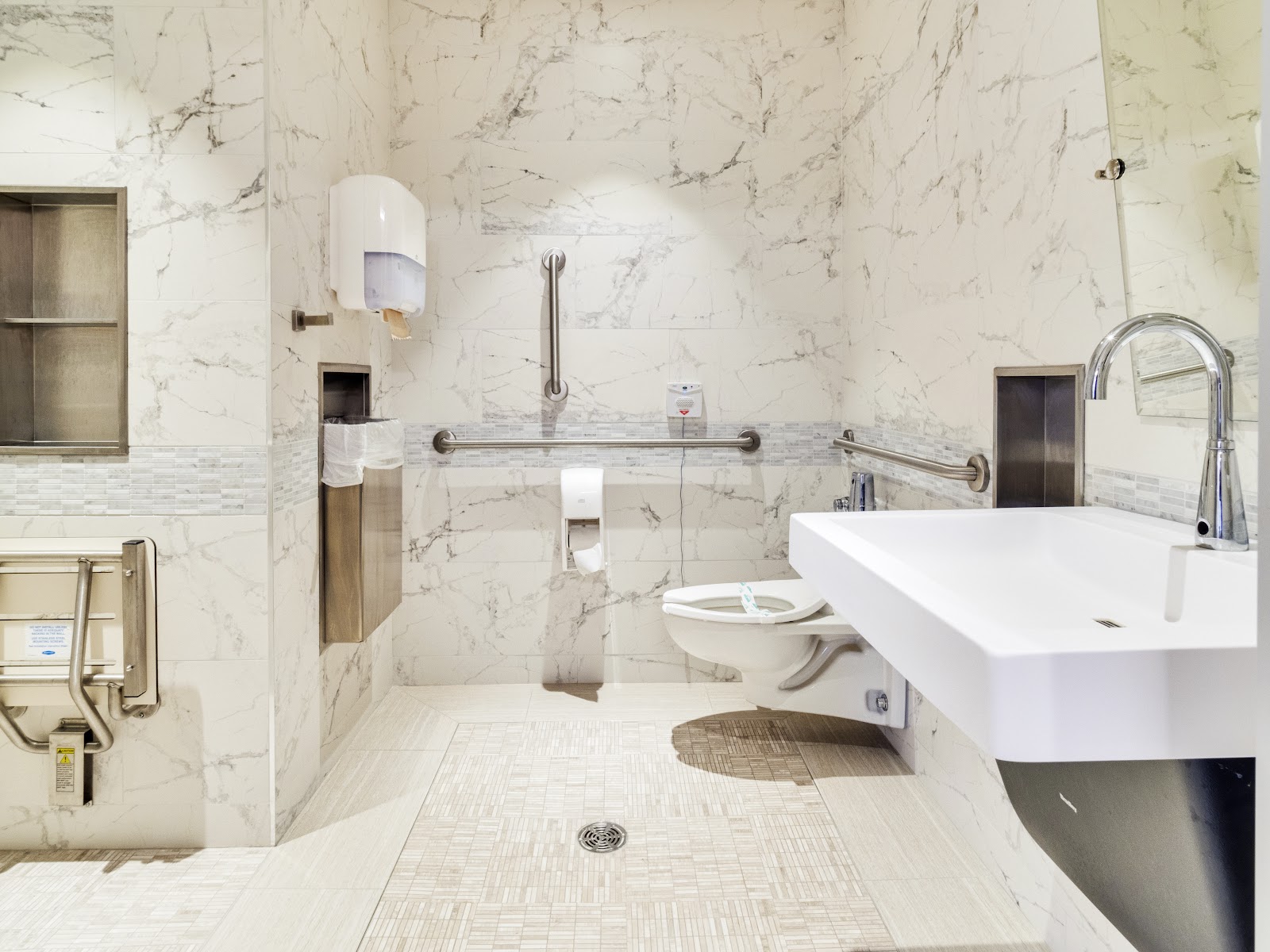 Modern bathroom with marble-effect tile walls, white rectangular sink, grab bars, and accessible features.