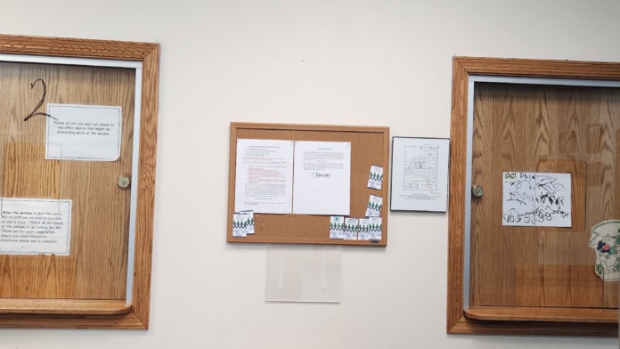 Interior wall with three cork bulletin boards displaying documents and notices, white walls, and reception desk area below