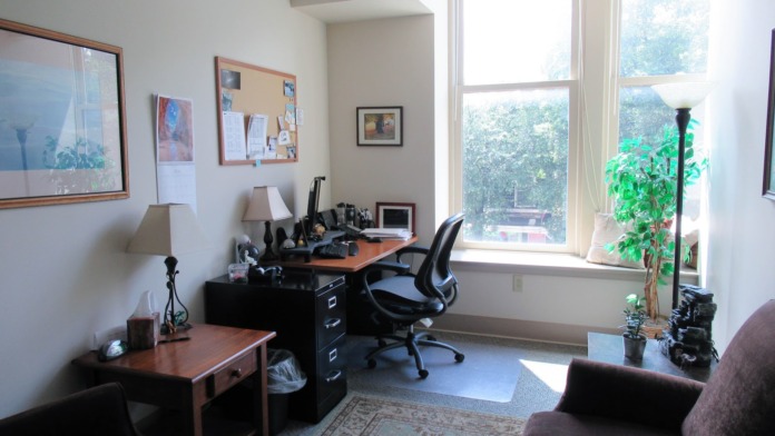 Interior office with desk, computer workstations, office chairs, windows with natural light, and wall artwork