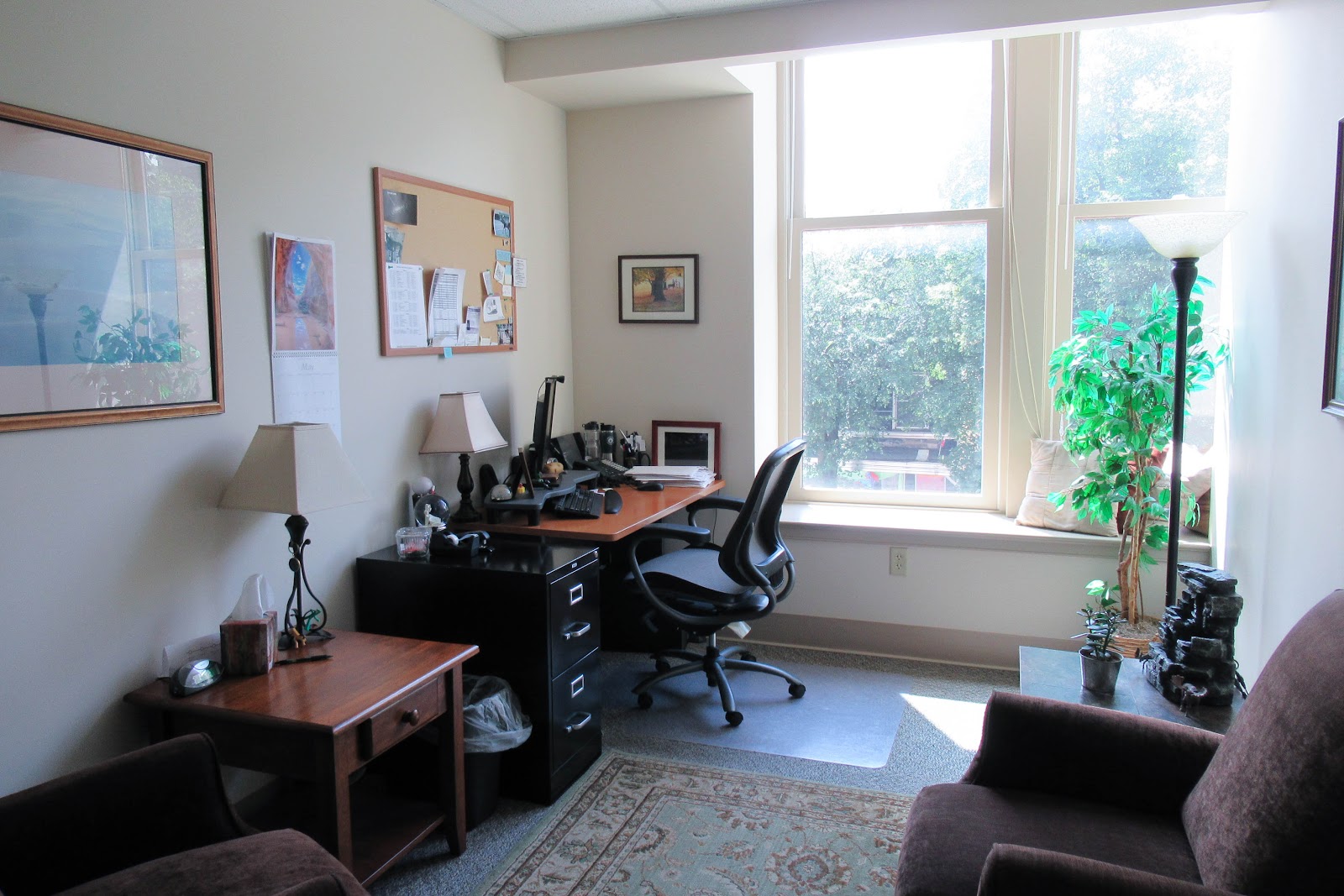 Interior office with desk, computer workstations, office chairs, windows with natural light, and wall artwork