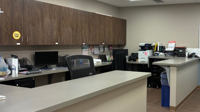Interior office workspace with desk counter, cabinetry, multiple workstations, computers, and overhead lighting