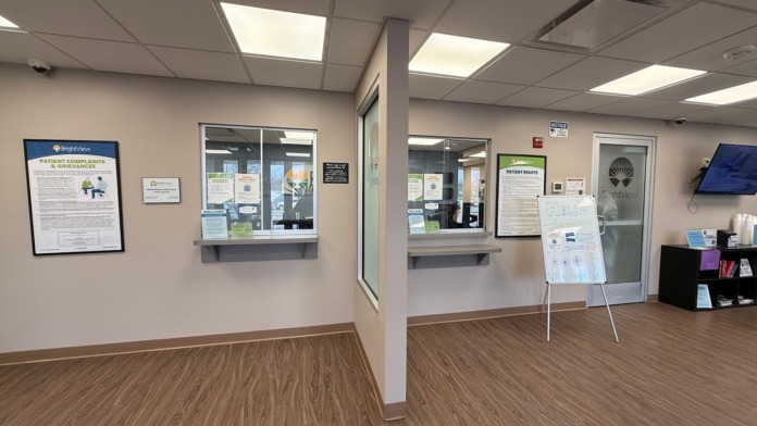 Interior administrative space with pale walls, brick detail, wooden flooring, information boards, and service window.