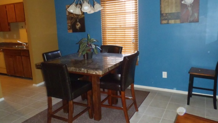 Interior dining space with round wood table, black chairs, blue accent wall, and pendant lighting fixture