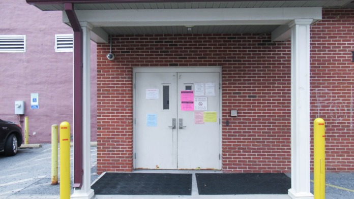 Exterior entrance with white double doors, yellow protective bollards, covered overhang, and brick construction