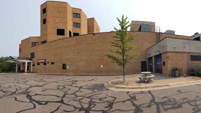 Brick facility building exterior with landscaped grounds, young tree, and picnic table in parking area