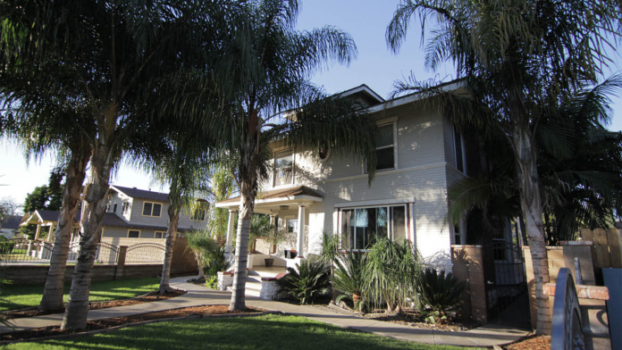 Two-story residential building surrounded by tall palm trees, green lawn, landscaping, and ornamental fencing.