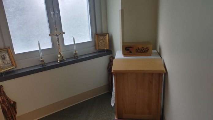 Interior chapel corner showing wooden cabinet, religious icons, candles, and frosted glass window