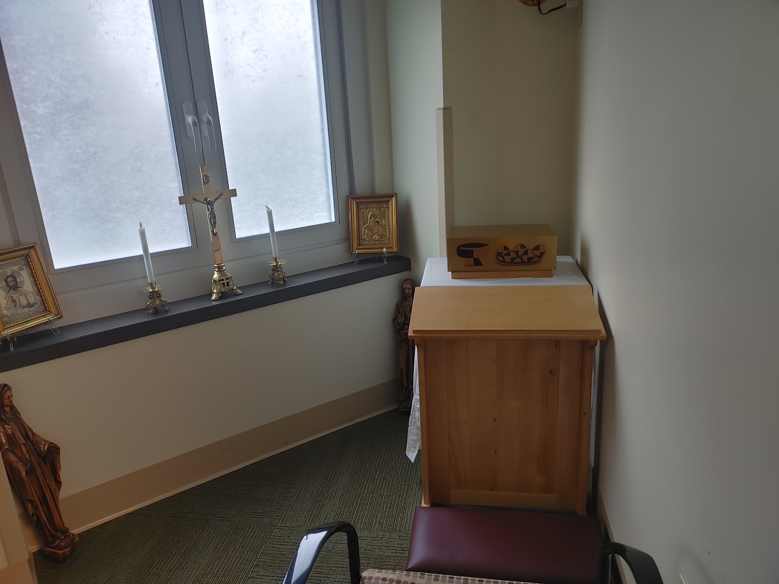 Interior chapel corner showing wooden cabinet, religious icons, candles, and frosted glass window