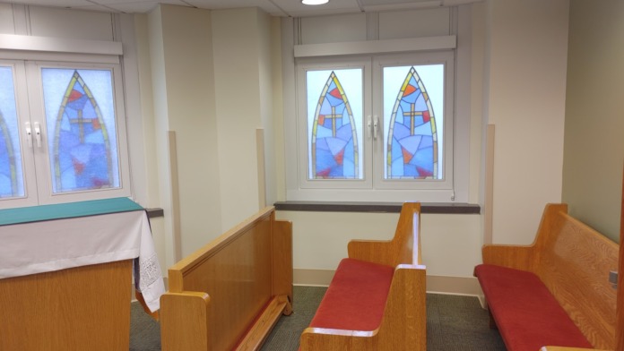 Interior chapel showing wooden pews with red cushions, stained glass windows, and altar furnishings