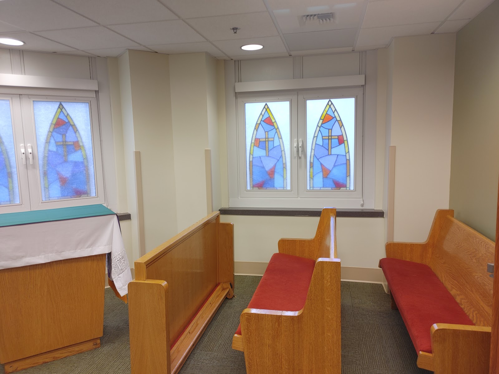 Interior chapel showing wooden pews with red cushions, stained glass windows, and altar furnishings