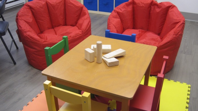 Interior playroom with red bean bag chairs, wooden activity table, colorful storage cubbies, and window view