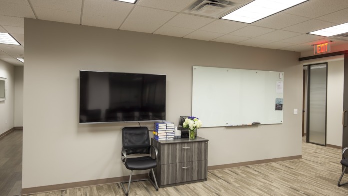 Interior training room with mounted television, whiteboard, instructor chair, desk, and fresh flowers