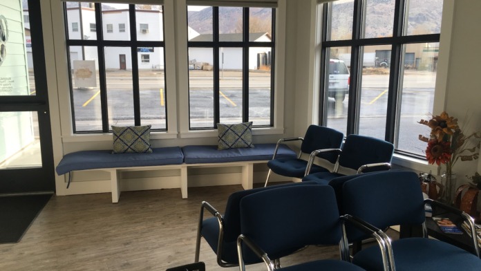 Interior waiting room with blue padded bench seating, blue chairs with metal frames, large windows overlooking parking, and seasonal decor.