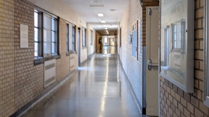 Interior hallway with directional signage, brick walls, fluorescent lighting, and clinical care area access