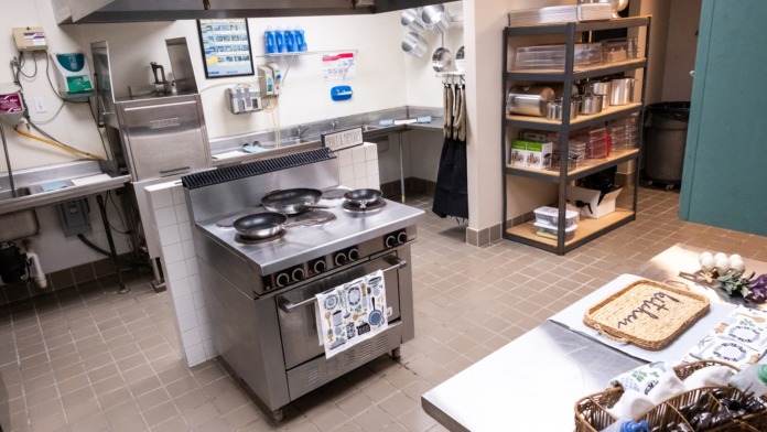 Interior kitchen with stainless steel cooking equipment, refrigeration, shelving, and food preparation counter space.