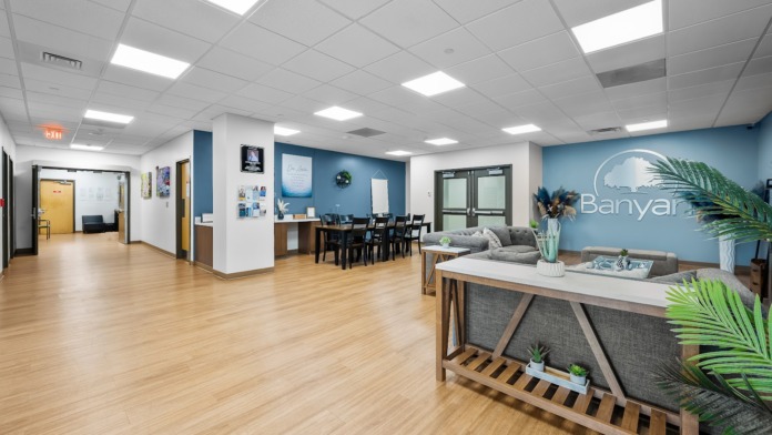 Interior lounge with blue accent wall, sofa, side table, potted plants, and Banyan branding