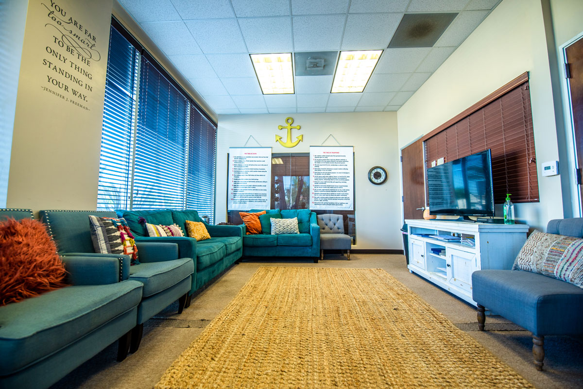 Interior common area with teal sectional sofa, yellow rug, windows, television, and nautical-themed blue wall decor