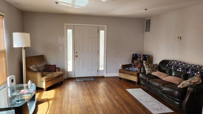 Interior living room with wood flooring, tan and leather furniture, glass coffee table, and natural lighting