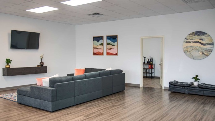 Open interior common area with sectional sofa, television, artwork, plants, and wood flooring
