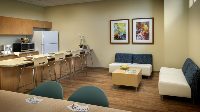 Interior common space with kitchenette, bar seating, lounge furniture, and framed wall art.