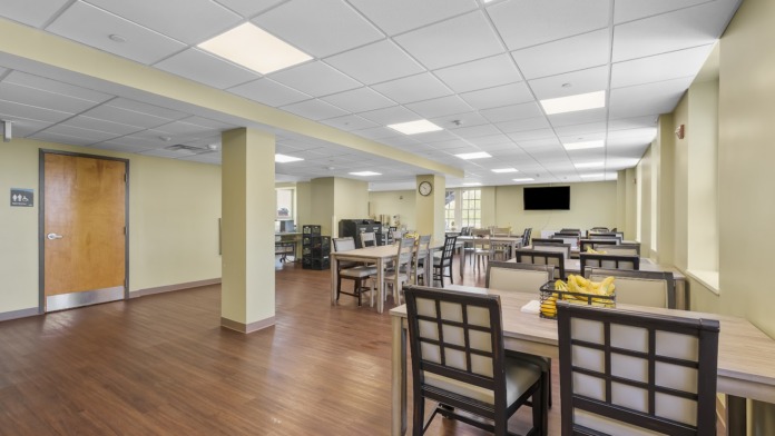 Interior dining space with multiple tables and chairs, wooden flooring, yellow walls, and recessed ceiling lighting