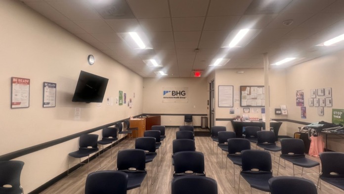 Interior room with arranged blue seating chairs, wall-mounted television, BHG branding, and professional meeting setup