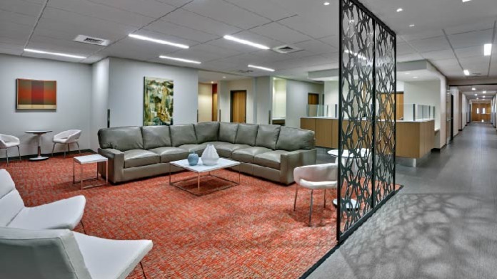 Interior common lounge space with large gray sectional seating, modern furniture, artwork, and geometric room divider.