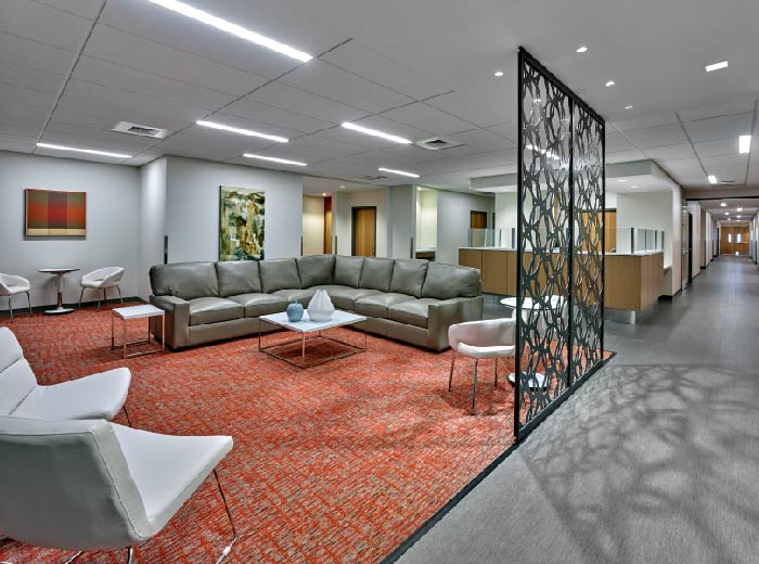 Interior common lounge space with large gray sectional seating, modern furniture, artwork, and geometric room divider.