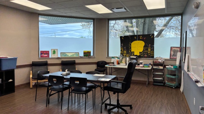 Interior meeting space with large windows, table, chairs, wood flooring, and wall artwork