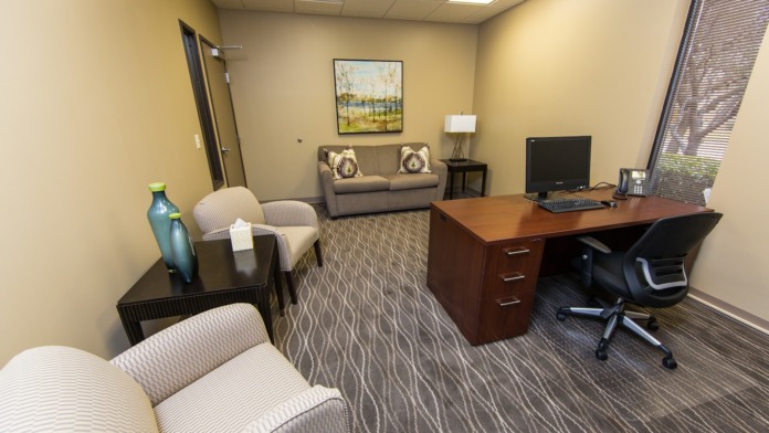 Interior office space with yellow walls, upholstered chairs, desk with computer, sofa, and framed landscape artwork.