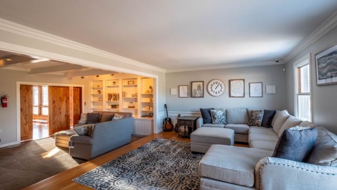 Interior living room with large sectional sofa, patterned area rug, built-in shelving, framed artwork, and wood flooring.