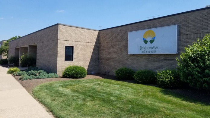 Tan brick exterior corner view with BrightView sign, manicured landscaping, lawn, and sky.