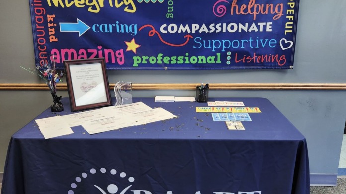 Interior display table with blue cloth, banner with motivational words, framed certificate, and facility branding materials