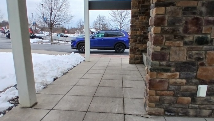 Interior covered entryway with tiled floor, brick pillar, glass doors, and view of parking area beyond.