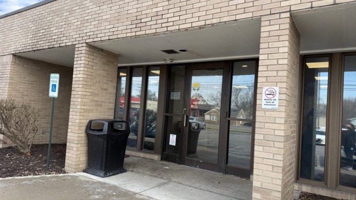 Exterior covered entrance with glass doors, brick walls, trash receptacles, and parking lot view.