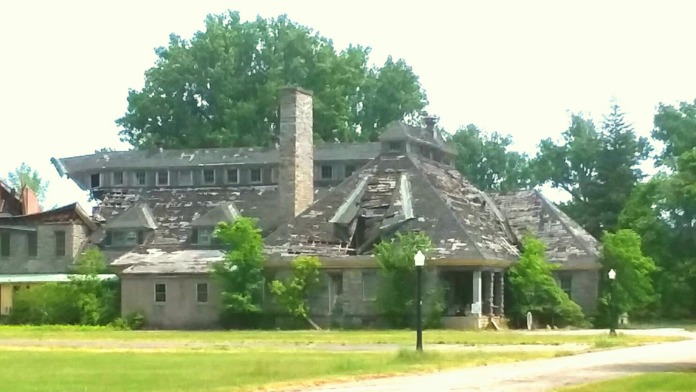 Exterior of large institutional building showing significant structural damage and roof deterioration across open grounds