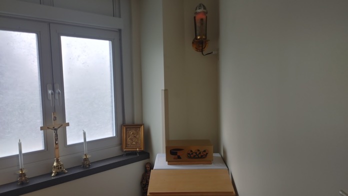 Interior alcove with wooden furnishings, religious icon, candles, and stained glass windows