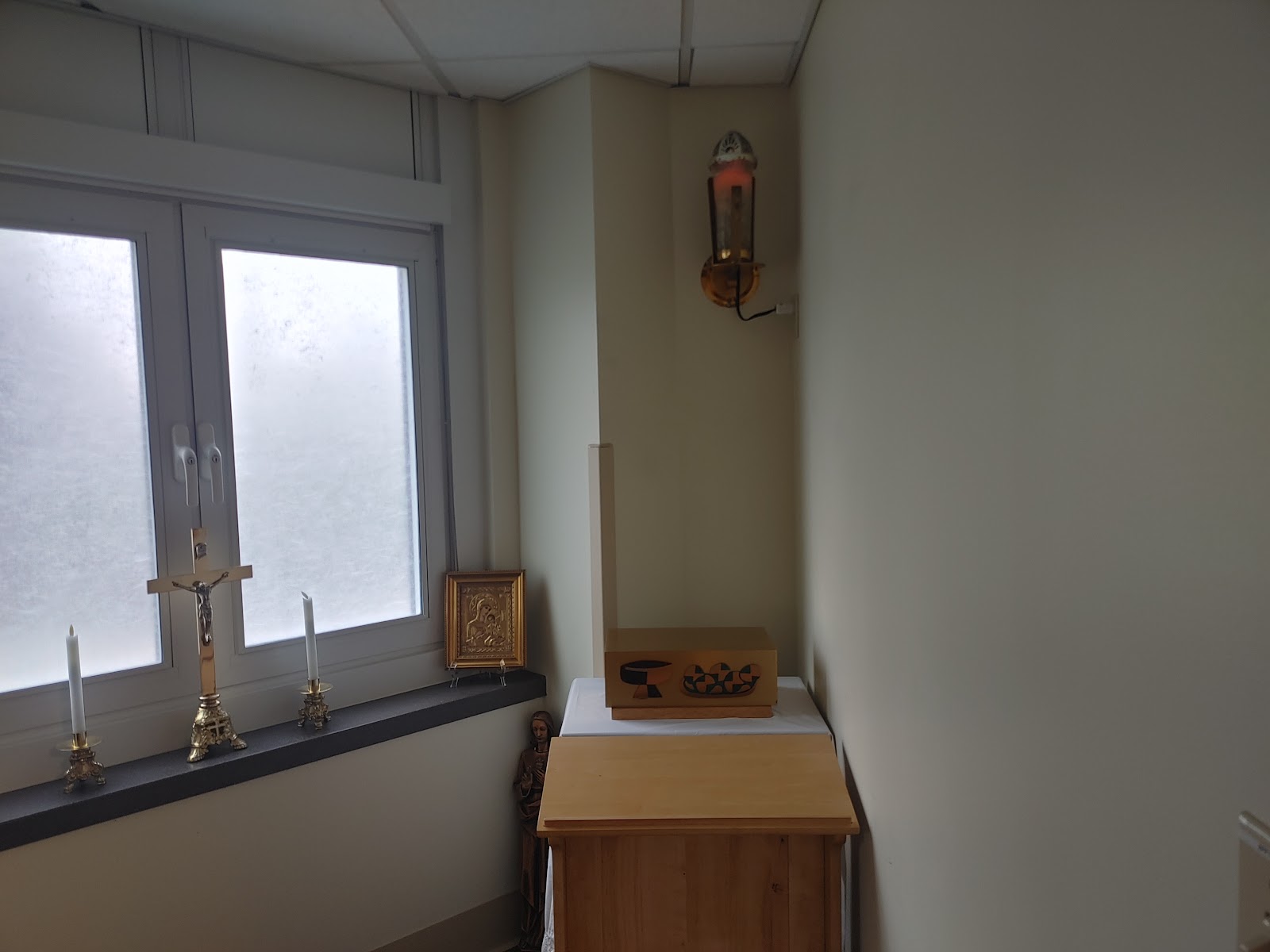 Interior alcove with wooden furnishings, religious icon, candles, and stained glass windows