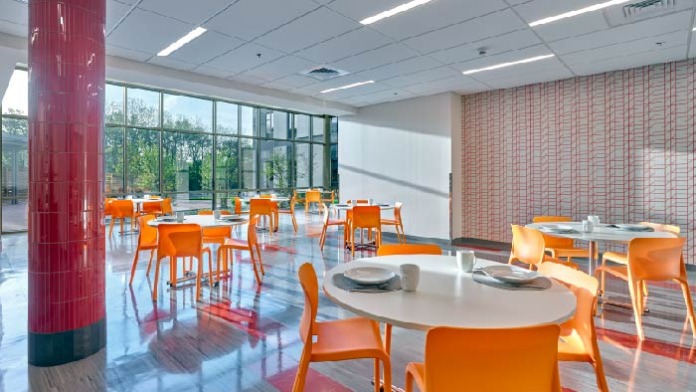 Interior dining space with modern seating, red cylindrical column accent, brick walls, and natural window lighting.