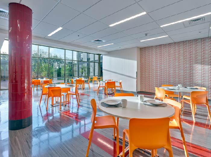 Interior dining space with modern seating, red cylindrical column accent, brick walls, and natural window lighting.