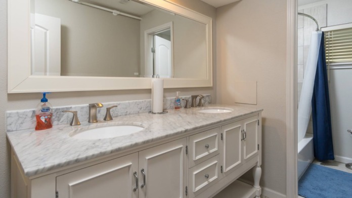 Bathroom with marble countertop, double sinks, white cabinetry, large mirror, and blue shower curtain