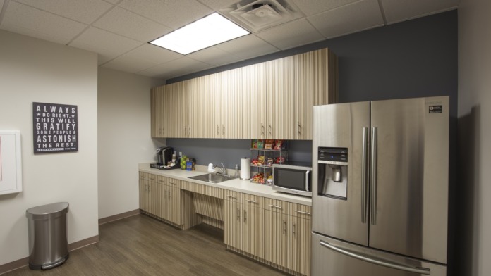 Interior break room featuring kitchenette with stainless steel appliances, wood cabinetry, and motivational wall signage