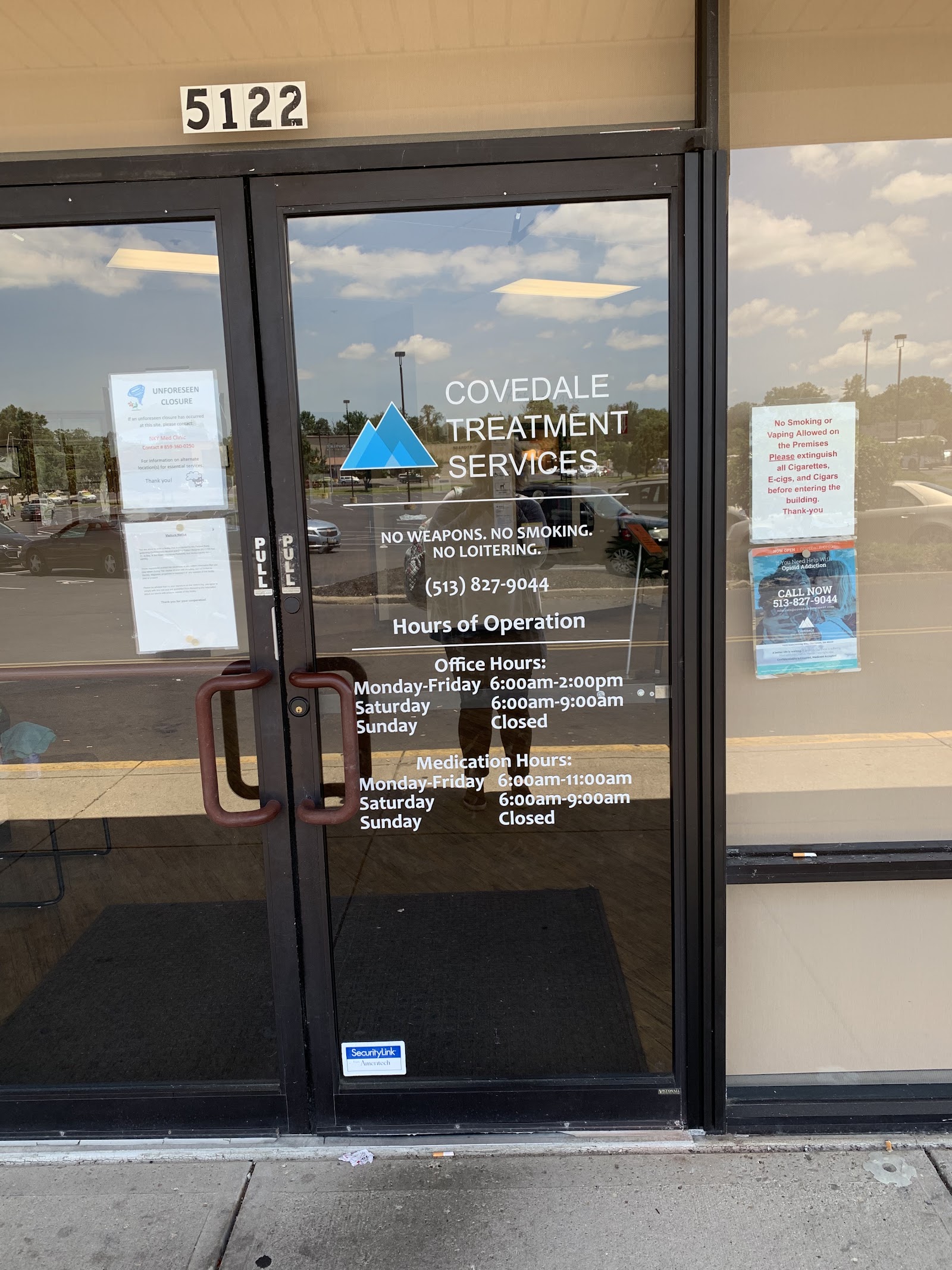 Interior entrance door showing facility address, hours of operation, policies, and contact information on glass