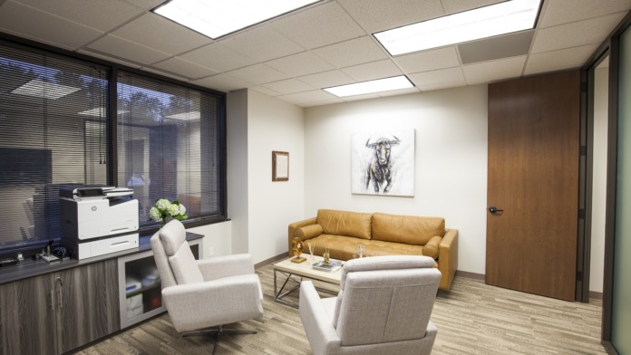 Interior office showing gold sofa, white armchairs, desk with printer, windows, and professional artwork