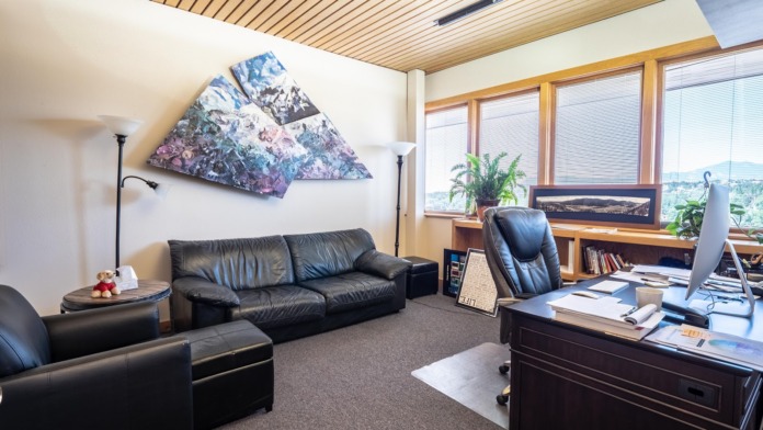 Interior office space with black leather furniture, desk, modern wall art, windows, and professional wood flooring.