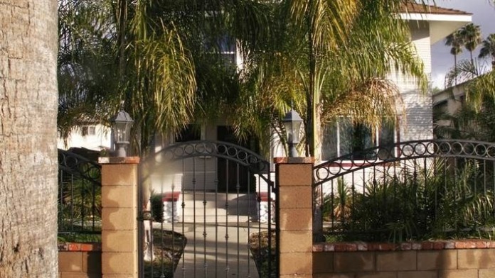 Ornamental metal gates with stone column accents framing entrance to palm tree-lined facility grounds.