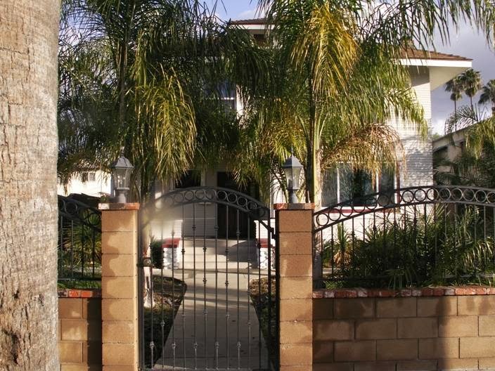 Ornamental metal gates with stone column accents framing entrance to palm tree-lined facility grounds.