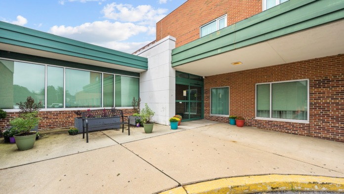 Outdoor patio area with brick building facade, green roof trim, benches, colorful planters, and concrete walkway