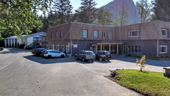 Exterior of treatment center showing cedar shake sided building, vehicles, landscaping, and mountain backdrop.